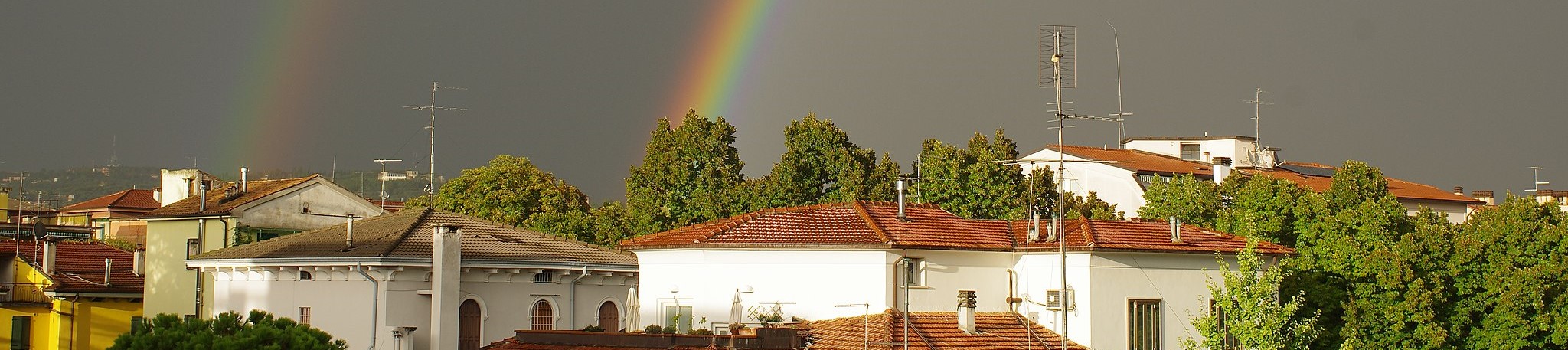 an image of Mediterranean houses with tiled roofs and a double rainbow behind them in the sky